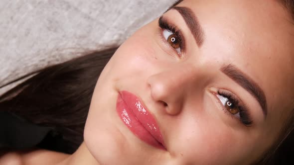 Beautiful Young Woman with Permanent Lip Make Up and Microblading Eyebrow Tattoo Lies with a Beauty