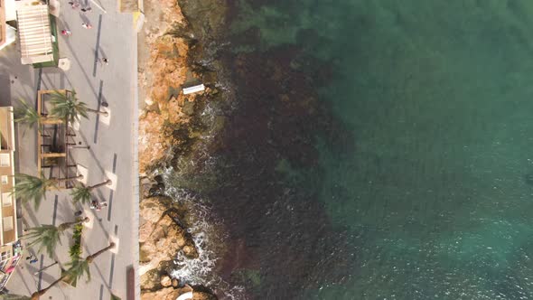 Tropical city coastline with people walking and majestic ocean water, aerial top down view