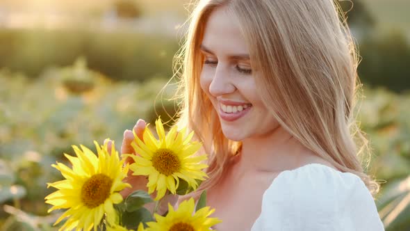 Girl Smells Bouquet of Sunflowers in the Field in Sunrays