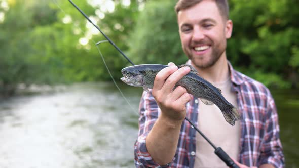 Fisherman Rests on the River and Catches Trout Smiles and Shows the Fish in the Camera