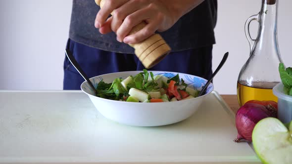 Man Grinding Pepper On Healthy Salad In Kitchen. - close up