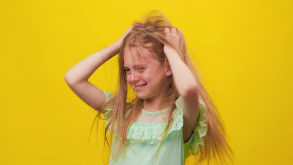 Unhappy Kid Girl Disheveled Scratch Hair on the Yellow Background