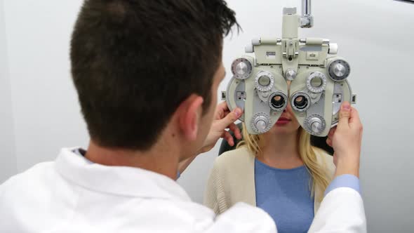 Smiling optometrist examining female patient on phoropter