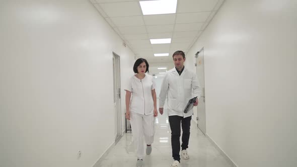 Doctors Man and Woman Walk Down the Corridor of Hospital and Discuss Patient's MRI Result