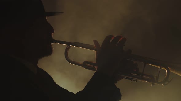 Silhouette of Man in Hat Plays Trumpet in Smoky Room Side View