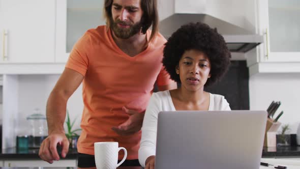 Mixed race couple using laptop and calculating finances in the kitchen at home