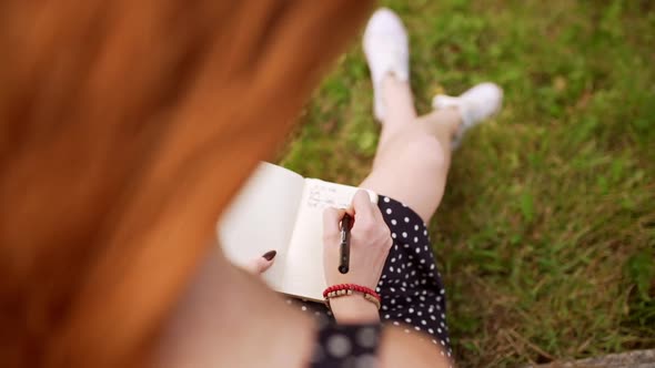 Caucasian Redhead Girl with Freckles on Shoulders Writing Notes While Camera Alternately Defocusing