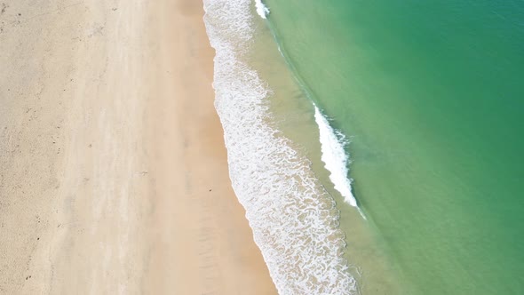 Waves of emerald colored sea breaking on golden sandy beach. Aerial top-down lowering