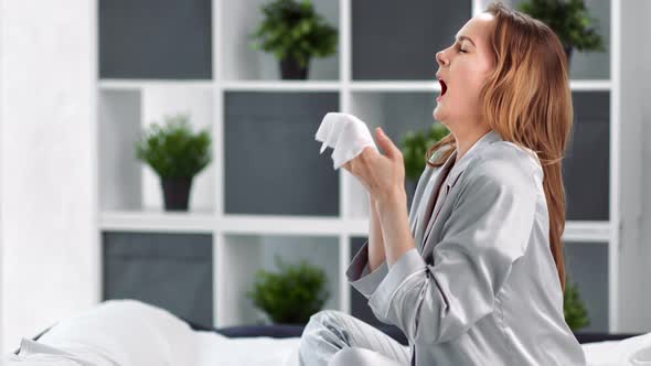 Sick Young Domestic Woman in Pajamas Sneezing in Tissue Having Flu