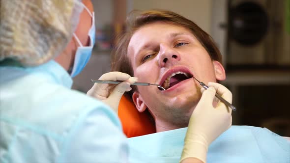 A Female Dentist Examines the Oral Cavity of a Patient with a Dental Mirror