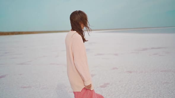 Walking Girl in Big Sweater and Blowing Pink Dress at Beautiful Landscape of Salt Flats at Pink Lake