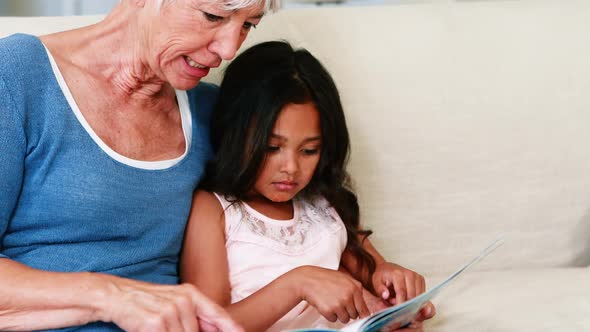 Grandmother and granddaughter interacting while looking at photo album in living room