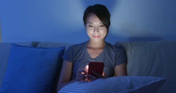 Woman use of mobile phone and sit on sofa at night