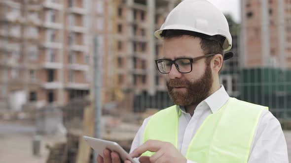 Portrait of a Successful Young Businessman Wearing a White Helmet in a Suit Working with Tablet