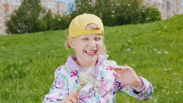 Blonde Girl in a Yellow Cap Playing with Dandelions