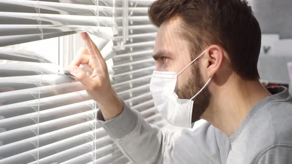 Man in Face Mask Peeking Through Window Blinds