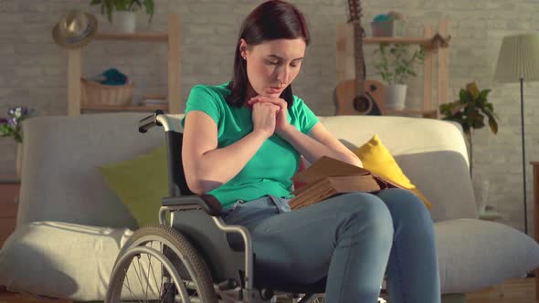 Young Disabled Woman Holding a Book and Reading a Prayer Sitting in a Wheelchair