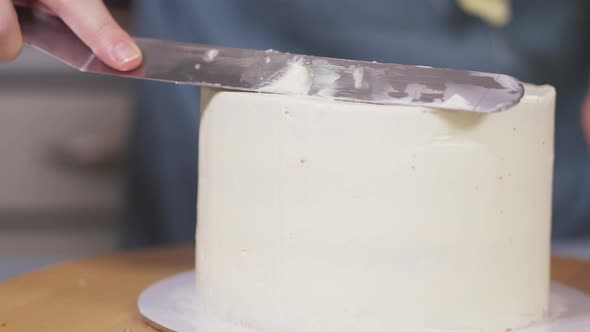 Woman Leveling a Light Cream on a Cake on a Rotating Stand in a Home Kitchen