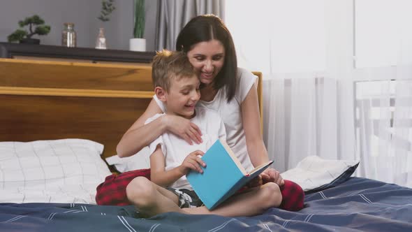 Woman and Her 8-Aged Son which Having Fun Together while Reading Book in the Bedroom