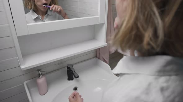 Rear View of Young Pretty Woman Wearing Pajamas Standing in Front of Mirror While Brushing Her Teeth