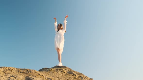Gorgeous Woman Stands on Top of Mountain in White Dress