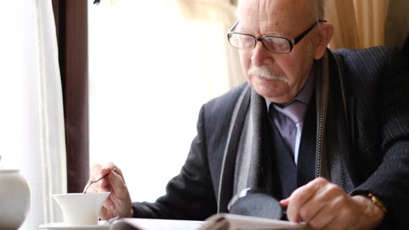 Portrait of an Old Grayhaired Grandfather with Glasses in Elegant Clothes He Reads the Newspaper