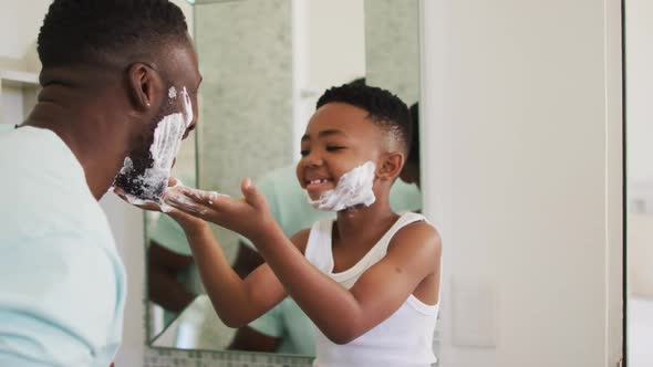 African american boy putting shaving cream on his father face and laughing together
