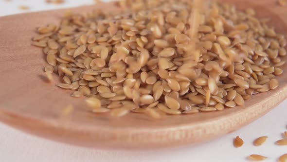 flax seeds fall in a heap on a wooden spoon on a white kitchen table 