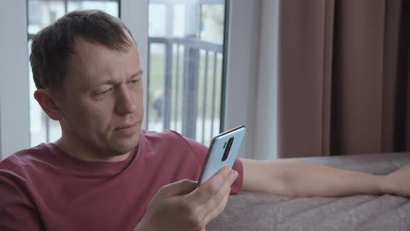 Man Reading Text Messages Surfing the Internet on Smartphone Sitting on the Couch