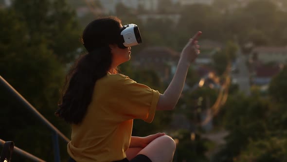 Young woman sits on the street in Vr glasses and interacts with a virtual display.