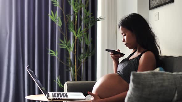 Young Pregnant Woman Sitting on the Sofa Taking Photos of Her Tummy Using a Smartphone