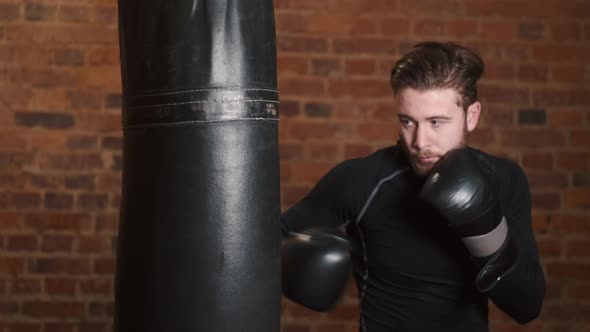 Dedicated Young Man Punching Boxing Bag at Gym