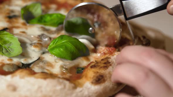 Slicing a hot and delicous homemade neapolitan pizza with basil and olives. Slowmotion close-up.