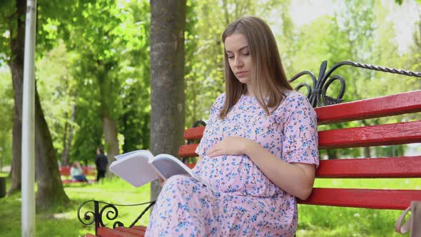 Pregnant Woman in a Summer Dress with a Floral Print Walks in the Park