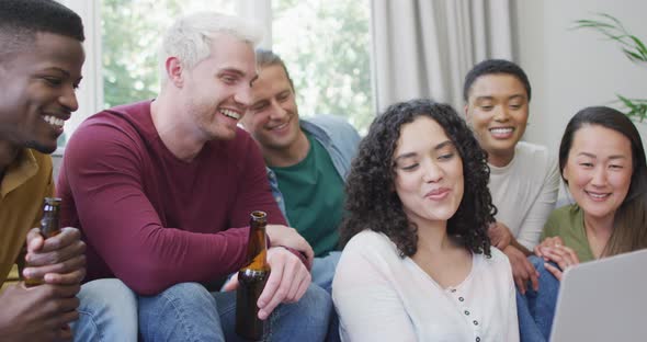 Diverse group of happy male and female friends looking at laptop and laughing in living room