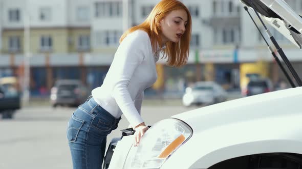 Young stressed woman driver near broken car with popped hood having a prbreakdown 