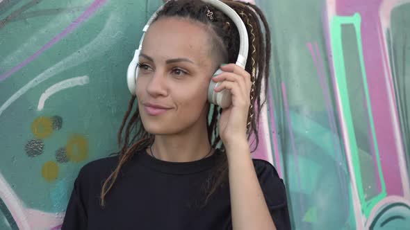 Modern Teenage Woman with Dreadlocks Listens to Music on Headphones