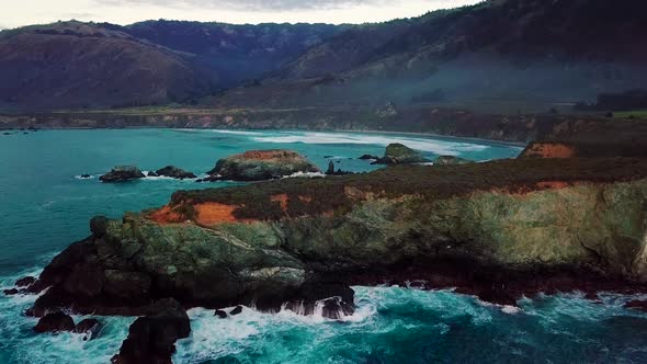 Flying over huge rocky cliffs and crashing waves at Sand Dollar Beach in Big Sur California at twili