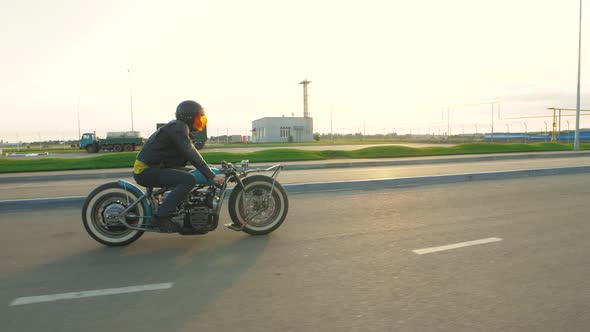 Young Man Biker with Custom Bobber Motorcycle on Street at Sunset