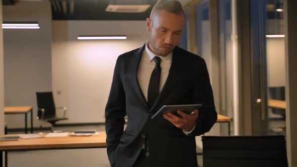 Young Man in Formal Suit Looking at Tablet PC at Evening Businesscentre.