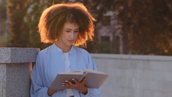 Afro American Woman Young African Girl Student Reads Book Sitting on Street Outdoors in Sun Lights