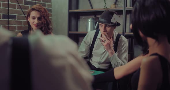 Young Man in a Hat Sits at a Gaming Table and Smokes a Cigar