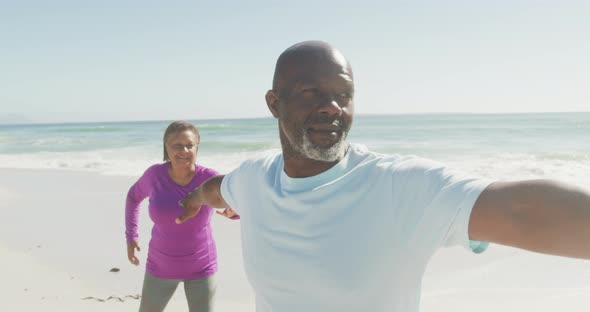 Smiling senior african american couple practicing yoga on sunny beach