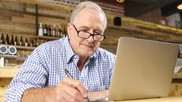 Senor man writing and using laptop in cafe 4k