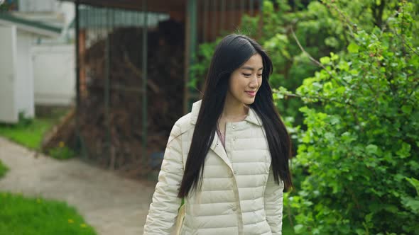 Young Smiling Woman Walking with Watering Can in Backyard Garden and Watering Green Bushes Outdoors