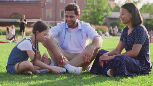 Multiethnic Parents and Adopted Daughter Sitting on Lawn in Park and Talking