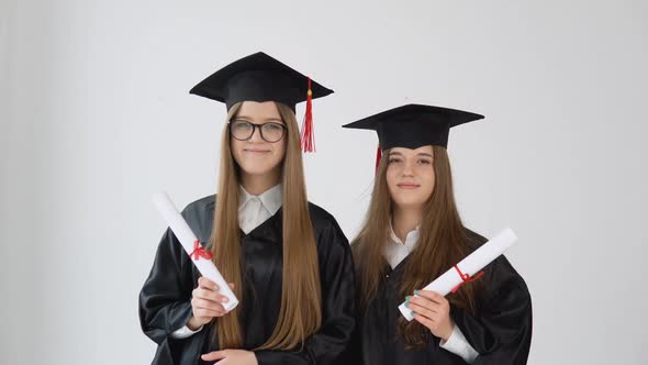 Two Young Happy Graduate Women Stand Shoulder to Shoulder with Graduating Diplomas in Their Hands