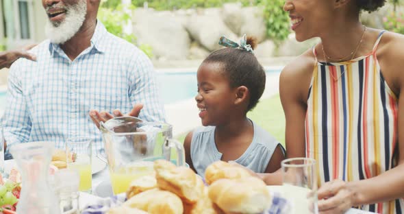 Happy african american family talking and having breakfast in garden