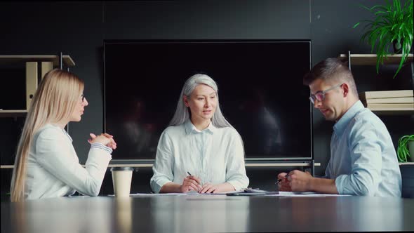 Senior Asian Female Mentor Talking to Younger Colleagues Interns in Office