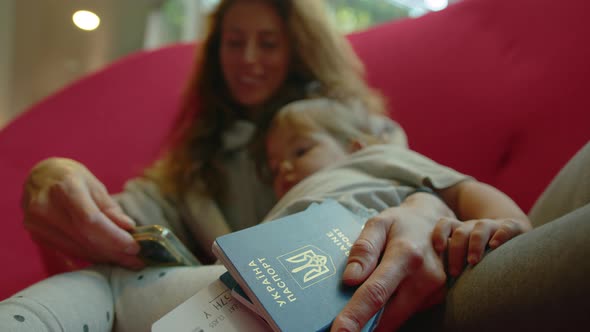 A Ukrainian Family is Sitting at the Airport in a Red Chair Waiting for Their Flight to Their